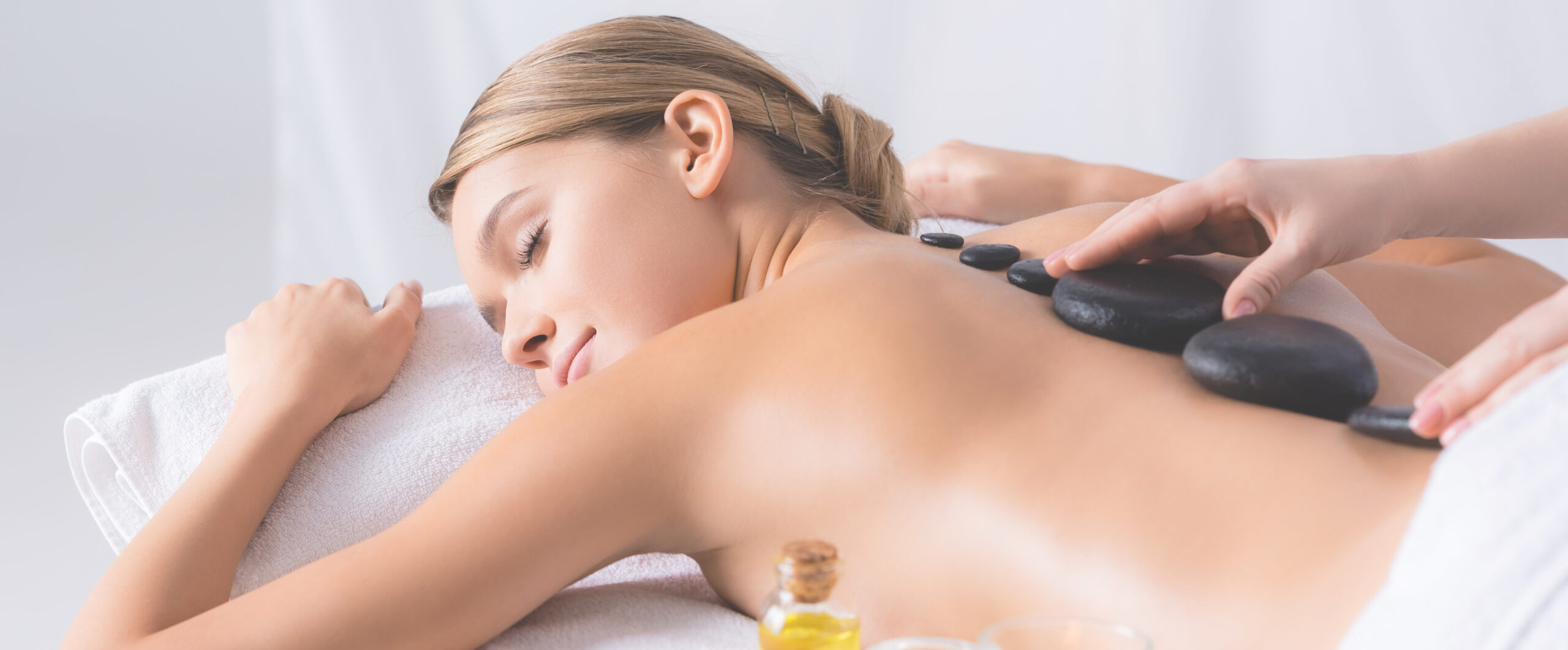 masseur doing hot stone massage to young woman with closed eyes